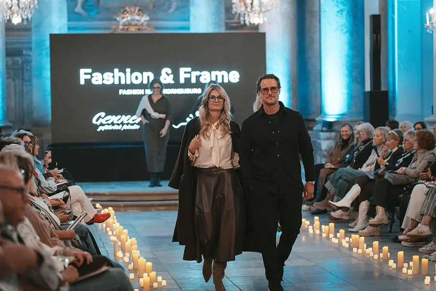 Zwei Models gehen nebeneinander vor der Leinwand, eines im langen Mantel