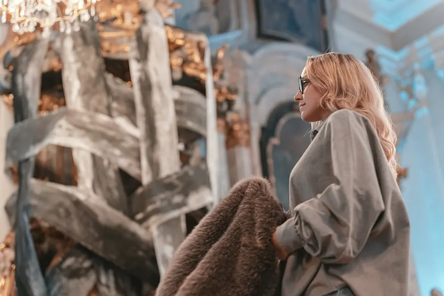 Model in grauem Oversize-Hemd mit flauschigem Mantel vor einer silbernen Skulptur