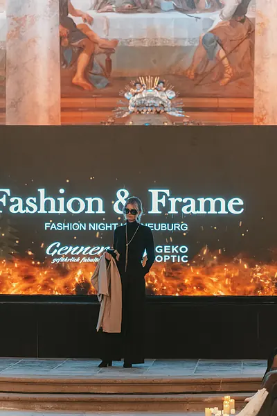 Model in Schwarz mit Camelmantel vor der Fashion-&-Frame-Leinwand mit Flammenmotiv