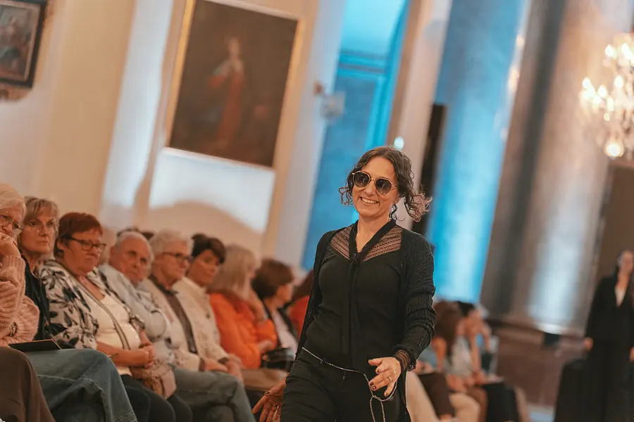 Lächelndes Model in schwarzer Bluse und Sonnenbrille geht am sitzenden Publikum vorbei