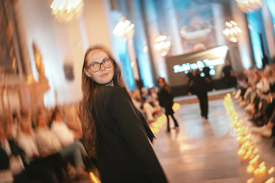 Model mit großer Brille und schwarzem Blazer blickt über die Schulter zurück