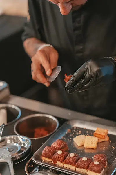 Person mit schwarzen Handschuhen richtet Häppchen auf einem Blech an