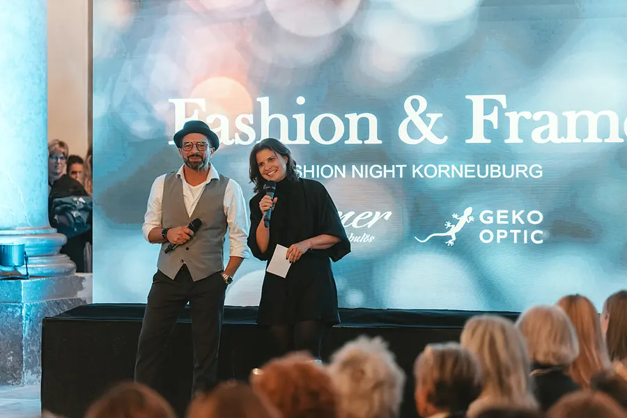 Zwei Personen mit Mikrofon auf der Bühne vor Leinwand und Publikum